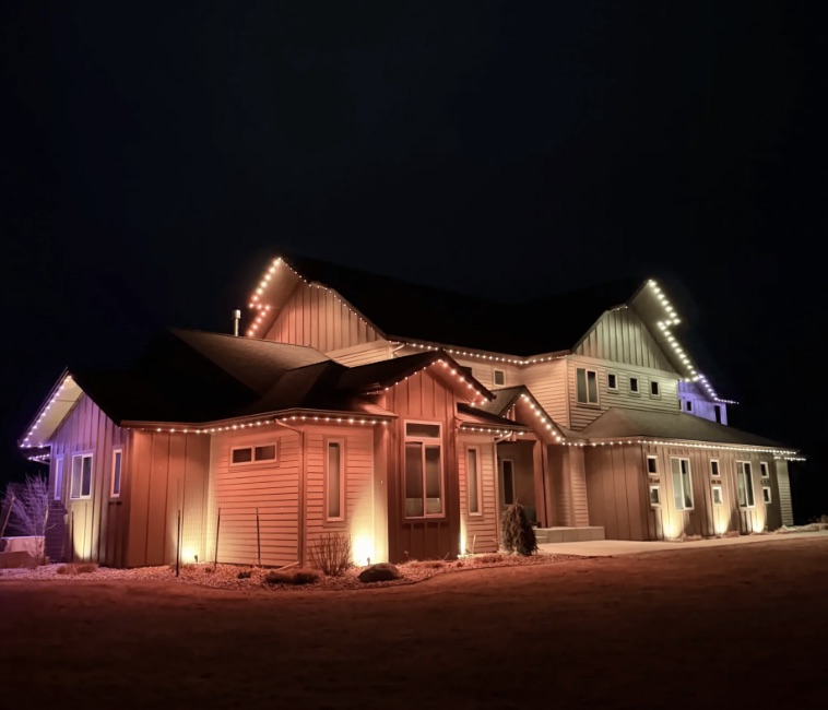Two-story farmhouse-style home with permanent lighting tracing every roofline and gable after dark