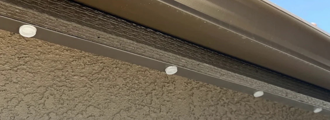 Daylight close-up of the permanent lighting track mounted flush beneath the fascia, color-matched to the brown trim with the individual LED lenses barely visible