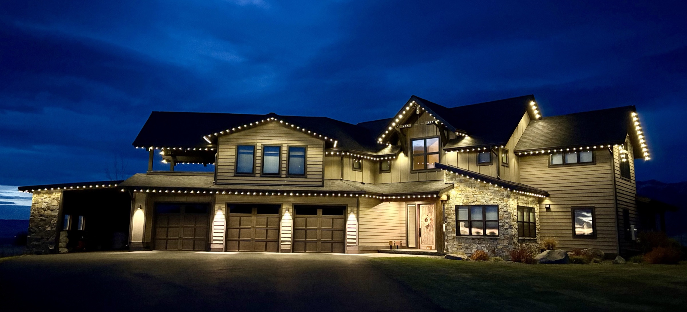 Large Montana craftsman home at blue hour with warm white permanent lighting along every roofline and gable
