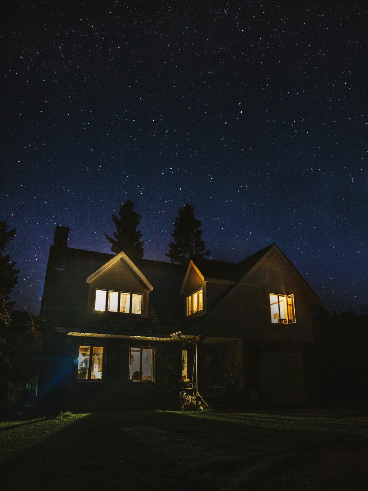 Two-story home with warm glowing windows under a starry night sky